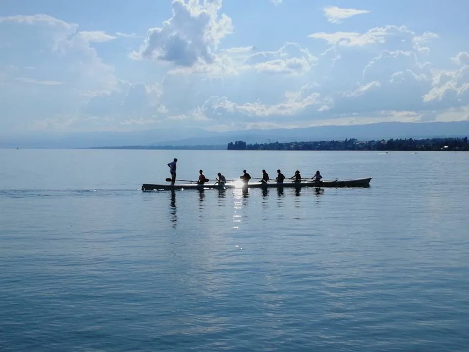 Backlit silhouettes of a crew gliding across Lake Geneva