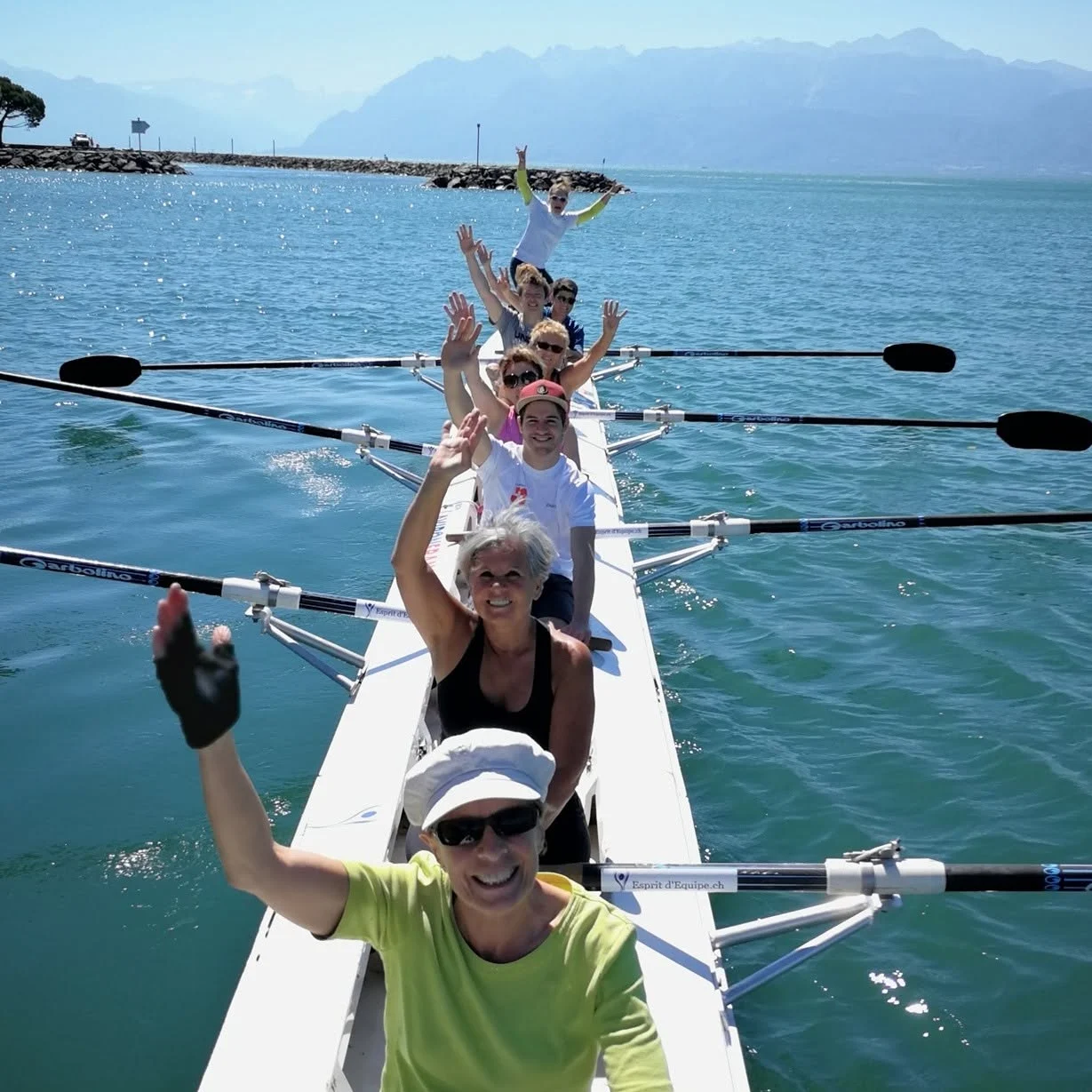 A cheerful crew waves from the boat on Lake Geneva, facing the Alps